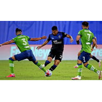 Andy Rios of the San Jose Earthquakes dribbles between two Seattle Sounders FC defenders
